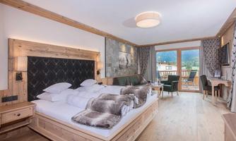 A modern hotel room with a large double bed and wood paneling. Large windows offer a view of the mountains.