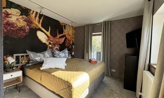 A modern bedroom with a large bed and stylish decor. A striking wall mural featuring a deer and flowers hangs on the wall.