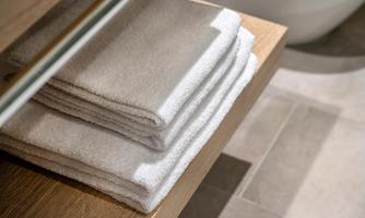 Clean, folded towels on a wooden shelf in the bathroom. The floor is in neutral tones.