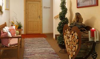 An inviting hallway with a wooden chair, cushions, and a colorful rug. Pictures are hung on the wall, and a decorative wooden heart with candles creates a cozy atmosphere.