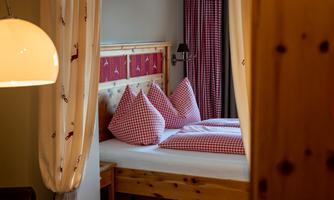 A cozy bedroom with a wooden bed and checked pillows. The walls are painted in warm tones, and the room feels inviting.