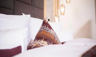 A cozy bed with white pillows and a decorative pillow in warm colors. The background is bright and modern designed.