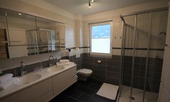 A modern bathroom with a large shower and two sinks. Bright tiles and a window create a friendly atmosphere.
