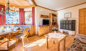 A cozy living room with wood details and a dining area. The room has large windows that let in plenty of daylight.