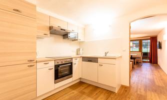 A modern kitchen with bright wood cabinets and a seamless floor. The room is well-lit and has an open access to the living room.