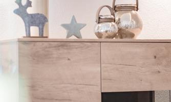 A modern wooden chest of drawers with decorative accessories. On it stand a blue deer, a star, and glass carafes.