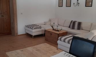 A cozy living room with a bright sofa, a wooden coffee tray, and a table. Pictures hang on the wall and there is a pleasant, inviting atmosphere.