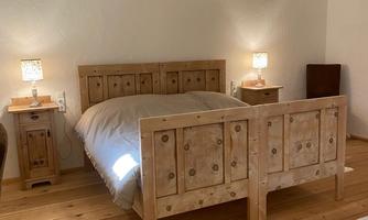 A cozy bedroom with a wooden bed and beige bedding. Next to the bed are two nightstands with lamps.