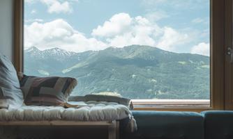 A cozy room with a view of green mountains and a landscape of clouds. The windows provide a clear view of nature.