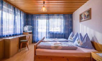 A cozy bedroom with two beds and blue curtains. The wooden ceiling and table give the room a warm atmosphere.