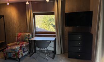A modern room with a colorful armchair, a table, and a television. Large windows offer a view of the landscape.
