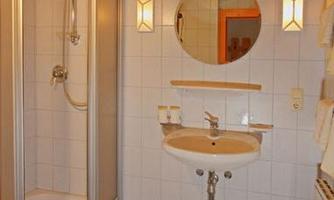 A modern bathroom with a shower stall and a sink. The walls are tiled and the floor has gray tiles.