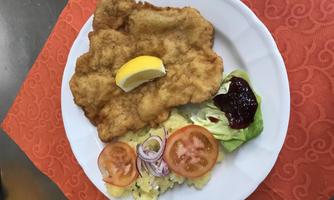 A plate with breaded schnitzel, garnished with a slice of lemon. Served with potato salad, fresh vegetables, and a salad.