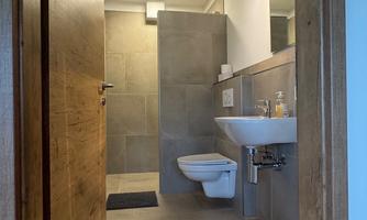 A modern bathroom with elegant tiles and a large mirror. The furnishings are simple and functional with a sink and a toilet.