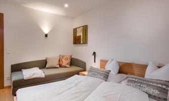 An inviting room with two beds and a cozy lounge area. The walls are painted light and the lighting is soft.