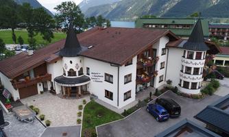A pretty hotel in alpine style with towers and balconies. Surrounded by picturesque mountains and a green landscape.