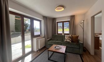 A bright living room with a comfortable sofa and a table. Large windows offer a view of nature outside.