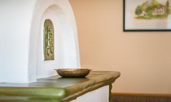 An elegant mantel with a decorative niche and a bowl made of bronze. In the background, there is an image of an idyllic landscape.