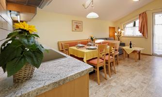 A bright and inviting room with a dining area and a modern kitchenette. Flowers and a bottle of wine are on the table, creating a cozy atmosphere.