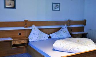 A cozy bedroom with a large bed and wooden furniture. The walls are decorated with pictures, and there are nightstands next to the bed.