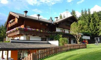 A beautiful house in the mountains with a large garden.  
Flowers decorate the balconies and trees surround the building.