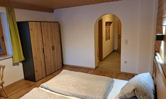 A cozy bedroom with a double bed and wooden paneling. In the background, a wardrobe and an archway area are visible.