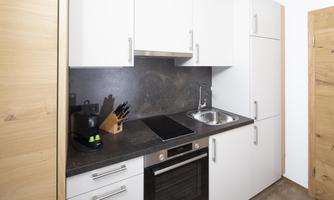 A modern kitchen with white cabinets and a dark countertop. It includes a stove, an oven, and a sink.