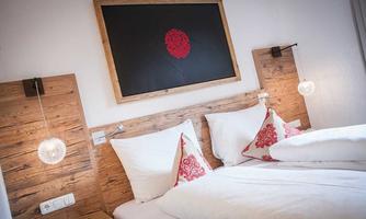 A cozy double room with wooden details and modern bedside lamps. The white bedspreads and pillows with red accents create an inviting atmosphere.
