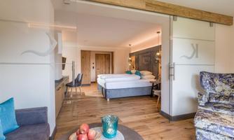A modern room with two beds and stylish decor. In the foreground is a table with fresh apples and a colorful vase.