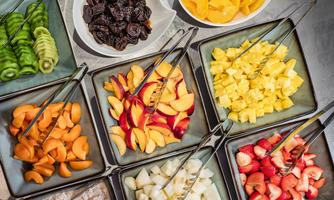 A colorful selection of fresh fruit in bowls, including kiwi, peaches, pineapples, and strawberries. There are also dried fruits like plums.