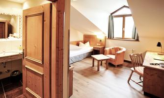 A cozy hotel room with wooden decor and a large window. There is a table, two chairs, and a bathroom in the background.