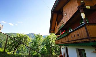 A traditional wooden house in the mountains with a beautiful view of the green hills. The sky is clear and sunny, ideal for a relaxing stay.