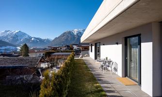Modern architecture with a spacious terrace and a view of snow-capped mountains. The sky is clear and blue, creating a relaxed atmosphere.