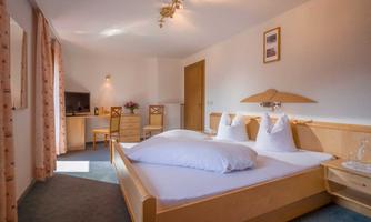 An elegant bedroom with a large bed and two pillows. The room is bright and cozy, equipped with a desk and a television.