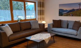 A cozy living room with a brown and a gray sofa.  
Generous windows provide a view of the mountains and an appealing wall decoration.