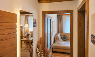 A bright hallway with wood paneling and a cozy sofa in an adjoining room. Daylight streams through the windows, creating an inviting atmosphere.