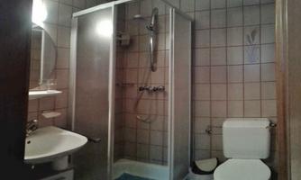 A simple bathroom with a shower cubicle and a sink. To the right is a toilet, and the walls are tiled.