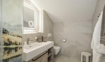 A modern bathroom with elegant furnishings and light, neutral colors. The decor includes a sink, a toilet, and a cozy stool.
