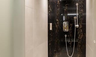 A modern shower with dark, marbled walls and a large rainfall showerhead. The floor is light and the lighting is pleasant.
