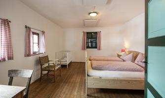 A bright room with two single beds and checkered bedding. The room has wooden floors and a cozy atmosphere with a table and chairs.