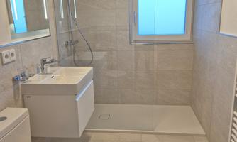 A modern bathroom with a shower and sink. It has bright tiles and a window that lets in daylight.