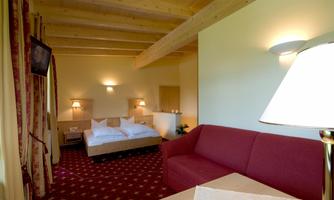 A cozy room with a double bed and a red sofa. The walls are bright, and the space has a warm, inviting atmosphere.