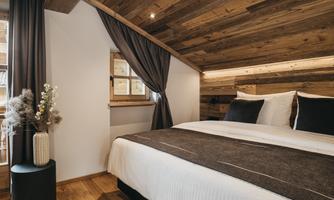 A cozy bedroom with wood paneling and modern accents. The bed is comfortable, and the windows let in a lot of light.