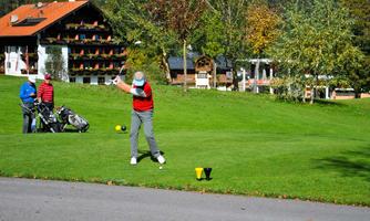 A golfer hits the ball on a beautiful golf course. In the background, trees and a building with balconies can be seen.