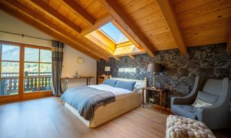 A cozy bedroom with a wooden beam ceiling and large windows. The room is bright and friendly with a modern bed and stylish decor.