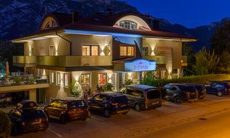 A beautiful hotel building at dusk. Several cars are parked in front of the house, and mountains can be seen in the background.