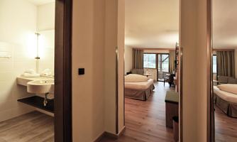 A modern hotel room with wooden floors and large windows. The bathroom is bright and well equipped.