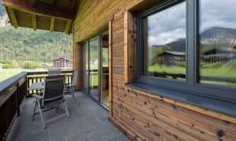 A cozy balcony with wooden cladding and modern furniture. In the background, green mountains and a peaceful landscape can be seen.