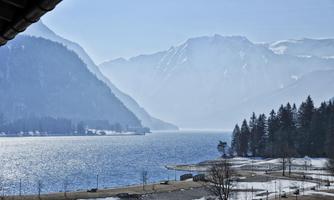 A picturesque lake surrounded by tall mountains. The landscape is calm and wintry, with a light mist over the water.