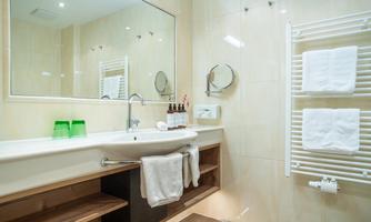 A modern bathroom with a large mirror and a bright, friendly design. Towels and toiletries are neatly arranged.